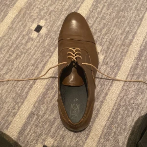 Bruna skinnskor med snörning, stl 47 - Stilrena bruna skinnskor från NeC med klassisk snörning och låg klack. Skorna har en spetsig tå och diskreta sömdetaljer längs sidorna. Perfekta för dig som vill ha en dressad look med en modern touch.      Du kan även se att dom är lite lite skadade på fram sidan men förutom de är jätte fina 