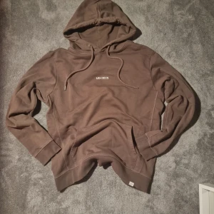 Brun hoodie från Les Deux, storlek L - Säljer en brun hoodie från Les Deux i storlek L. Tröjan har huva med snörning, magficka och diskret Les Deux-tryck på bröstet. 