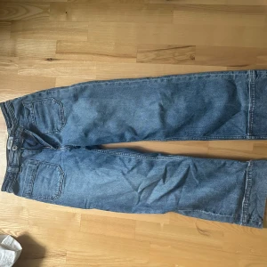 Blå raka jeans med hög midja - Säljer ett par klassiska blå jeans med raka ben och hög midja. Jeansen har två stora bakfickor och stängs med knapp och dragkedja. Perfekta för en avslappnad och stilren look.