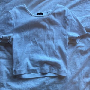 Vit croppad topp från Gina Tricot - Enkel och stilren vit croppad topp från Gina Tricot. Modellen har rund halsringning och korta ärmar. Perfekt att matcha med jeans eller kjol för en clean look. Tillverkad i mjuk bomull som känns skön mot huden.