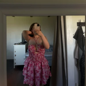 Somrig klänning - Supersöt kortklänning i rosa och vitt med blommigt mönster och volangkjol. Klänningen är axelbandslös men har även möjlighet till halterneck med knyt.  Passar perfekt till sommaren!😍