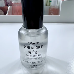 Snail Mucin 95 + Peptide Facial Essence - Essence med 95% snigelsekret och peptider från Jumiso. Kommer i en genomskinlig glasflaska med svart pump. Produkten är parfymfri och icke-komedogen, perfekt för att lugna och återfukta huden.