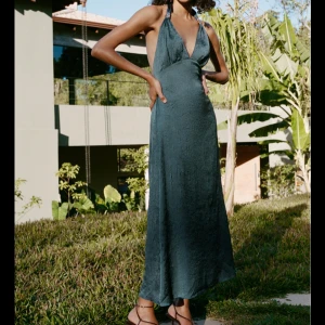 Zara långklänning  - Säljer en elegant petroleum långklänning med halterneck och djup v-ringning. Klänningen har öppen rygg och är tillverkad i ett glansigt, mjukt material som ger en lyxig känsla. Kontakta mig för egna bilder 🫶🏼