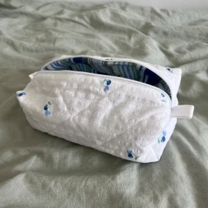 Necessär - Superfin vårig necessär med blåa körsbär och randigt tyg på insidan, perfekt för smink eller hudvård. 🫐🩵 Måtten är cirka:     Höjd: 10cm     Längd: 21cm     Bredd: 11cm