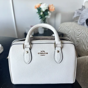 Vit handväska från Coach - Säljer en stilren vit handväska från Coach med guldfärgade detaljer och dubbla handtag. Nyskick.