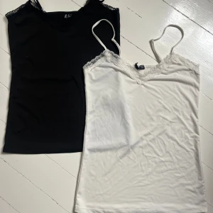 Svart och vit linnetoppar med spets i lent material - Två stilrena linnetoppar i svart och vitt med smala axelband och spetsdetaljer vid urringningen från Pieces. Perfekta att bära under en skjorta eller som de är. Mjukt och lent material som känns skönt mot huden. Inte så använda, men har växt ur så kan inte använda. Skriv för fler bilder💞