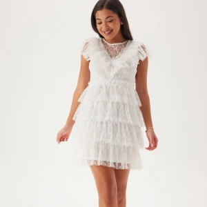 Studentklänning - Helt ny och oanvänd klänning (prislappen är kvar original pris 899 kr). Superfin vit kortklänning i spets med flera lager volanger och v-ringad hals. Klänningen har korta ärmar och pärlknappar i ryggen. Perfekt för studenten!!🌟🌟