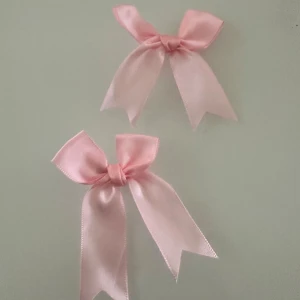 Rosa rosett hårspännen - Två söta hårspännen med ljusrosa rosetter i satinband. Perfekta som accessoar för att piffa upp frisyren. Rosetterna har metallspänne på baksidan för enkel användning.