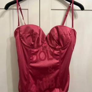 Rosa korsettopp från Dolce & Gabbana - Säljer en snygg rosa korsettopp från Dolce & Gabbana med justerbara axelband och markerade kupor. Toppen har diskret logotypmönster framtill och knäppning med hyskor bak. Perfekt för att lyfta vilken outfit som helst!