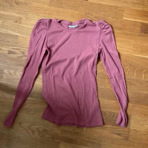 Rosa ribbad långärmad topp från Name It - Säljer en rosa ribbad långärmad topp från Name It. Tröjan har puffade axlar och en tight passform som sitter snyggt på kroppen. Perfekt för dig som gillar en enkel men trendig stil.