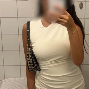 Vit omlottklänning från Zara - Säljer en elegant vit omlottklänning från Zara. Klänningen har en tight passform, är ärmlös och har fina draperade detaljer längs sidan. Perfekt för dig som gillar stilrena och trendiga plagg. Materialet känns mjukt och följsamt.