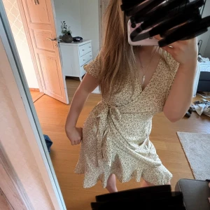Omlottklänning från Vero Moda - Supersöt ljusgul omlottklänning från Vero Moda i storlek XS💛Klänningen har blommiga detaljer och band som knyts i midjan. Perfekt till sommaren💕Använd endast ett fåtal gånger.