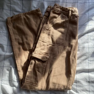 Beiga/Khaki lågmidjade cargopants - Säljer ett par beiga/khaki cargopants med raka ben och flera fickor, inklusive en klassisk cargoficka på sidan. Byxorna har normal passform och i storlek M. Perfekta för en avslappnad och trendig stil. Från Shein💕