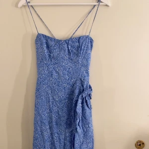Blå klänning med smala axelband från Zara - Säljer en lång blå klänning från Zara med smala axelband och vitprickigt mönster korsad i ryggen. Klänningen har en figurnära passform och en slits på sidan. Perfekt för varma dagar och somriga tillfällen. Skriv för mer bilder!! Ny pris 399kr