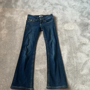 Blå bootcut jeans från Gina Tricot - Säljer ett par klassiska blå jeans från Gina Tricot med bootcut-modell. Jeansen har låg midja, fem fickor och tydliga kontrastsömmar. Perfekta för dig som gillar en trendig och cool look