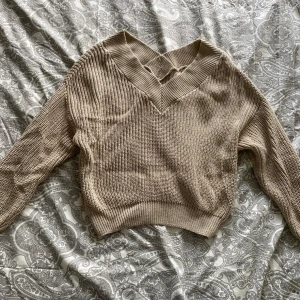 Beige stickad croppad tröja från NA-KD - Säljer en beige stickad tröja från NA-KD med v-ringad hals och croppad passform. Tröjan har långa ärmar och bred ribbad mudd vid midjan och ärmslut. Perfekt för lager-på-lager och snygg till jeans eller kjol.