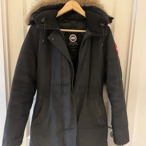 Svart parkajacka  Canada Goose Victoria parka - Säljer Victoria parka  Canada Goose med  päls. Jackan har dragkedja och knappar framtill, två innerfickor. Jackan är rökfri men har dock inte kemtvättat den. Har en super liten defekt vid ärmen annars är den felfri 🫶🏽