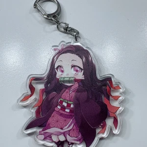 Anime nyckelring med Nezuko - Söt nyckelring med en chibi-version av Nezuko från Demon Slayer. Motivet har rosa och lila toner, med detaljer som röd kimono och grönt bamburör. Perfekt accessoar för animefans!