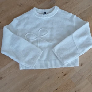 Vit stickad tröja - Superfin vit stickad tröja från Divided med croppad passform. Framsidan har en söt rosettdetalj i samma material. Lite nopprig/luddig men annars inga deffekter.