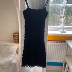 Svart axelbandsklänning från ONLY - Säljer en svart axelbandsklänning från ONLY. Klänningen har smala axelband och är täckt av flera lager volanger som ger en snygg struktur. Perfekt för dig som vill ha en stilren men ändå unik look.