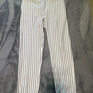 Vita randiga byxor med raka ben - Snygga vita byxor med svarta vertikala ränder och raka ben. Byxorna har hällor för bälte, knapp och dragkedja framtill. Perfekta för en stilren och trendig look. Köpt utomlands