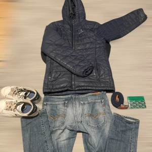 Svart quiltad pufferjacka från U.S. Polo Assn. - Svart quiltad pufferjacka med huva från U.S. Polo Assn. Jackan har dragkedja framtill, två sidofickor och broderad logga på bröstet. Perfekt för kyliga dagar och enkel att matcha med olika outfits,den har dock ett hål där bak