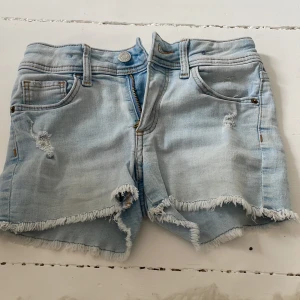 Ljusblå jeansshorts med fransar från H&M - Säljer ett par ljusblå jeansshorts från H&M med slitna detaljer och fransig kant. Shortsen har klassisk femficksdesign, dragkedja och knapp framtill. Perfekta för en avslappnad stil till sommaren 💕Tvättar så klart produkten innan jag skickar den😊