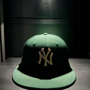 Grön New Era keps med NY-logga - Mörkgrön keps från New Era med broderad vit NY-logga framtill och 1999 World Series-märke på sidan. Klassisk flat peak och broderad MLB-logga baktill. Perfekt för dig som gillar sportig streetstyle.