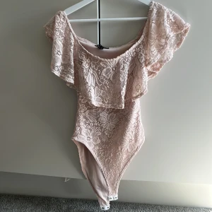 Ljusrosa spets offshoulder bodysuit - Säljer en ljusrosa bodysuit med spets. Den är köpt på plick och aldrig använd då den inte passsde❤️❤️ super fint skick och unik🥰