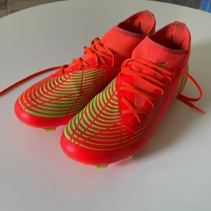 Adidas Predator fotbollsskor i orange och neon - Säljer ett par Adidas Predator fotbollsskor i en riktigt snygg orange färg med neongröna detaljer och mönster. Skorna är använda men mycket bra skick. Knappt något slitage på dobbar och luktfria och har rndast använt ett fåtal gånger.