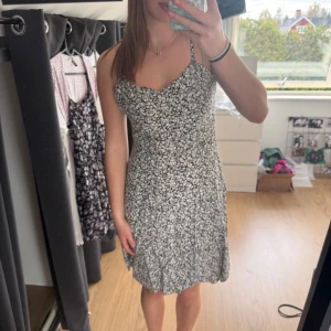 Svartvit blommig klänning - Säljer en svart klänning med vita små blommor och smala axelband. Klänningen har en lätt utställd passform och är i kort längd, perfekt för varma dagar. Materialet är jätteskönt! Knappt använd alls. Nypris: 300kr