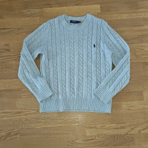 Ljusgrå kabelstickad tröja från Polo Ralph Lauren Stl S - Säljer en klassisk ljusgrå kabelstickad tröja från Polo Ralph Lauren med rund halsringning och broderad marinblå logga på bröstet. Perfekt för en stilren och tidlös look. Ulltröja från ralph lauren nypris ca 2500kr mitt pris 799kr. Priset är inte hugget i sten.