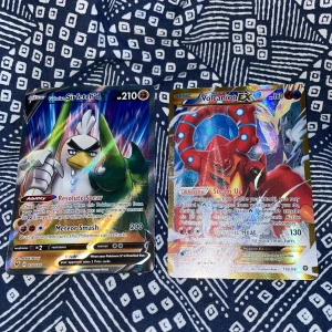 Pokémonkort: Galarian Sirfetch’d V och Volcanion EX - Två Pokémonkort säljes: Galarian Sirfetch’d V med 210 HP och Volcanion EX med 180 HP. Båda korten är holografiska och har färgstarka illustrationer. Perfekt för samlare eller Pokémon-fans som vill stärka sin kollektion.