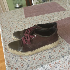 Vinröda sneakers med snörning - Säljer ett par vinröda sneakers från lanvin med snörning och rund tå. Skorna har ovandel i mocka och tåparti i blankt material.  Perfekta för en avslappnad stil.