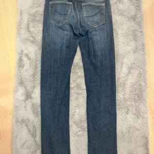 Jacob Cohen blå jeans straight fit - Snygga blå jeans från Jacob Cohen med klassisk straight fit och kontrastsömmar. Byxorna är tillverkade i en mjuk bomullsdenim med lite stretch för extra komfort. Insidan har rutigt tygdetalj och etiketter som visar att de är handgjorda i Italien.