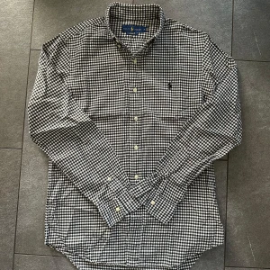 Svartvit rutig skjorta Ralph Lauren - Snygg svartvit rutig skjorta från Ralph Lauren i bomull, custom fit. Skjortan är i gott skick men och har ett nypris på ca 1500kr
