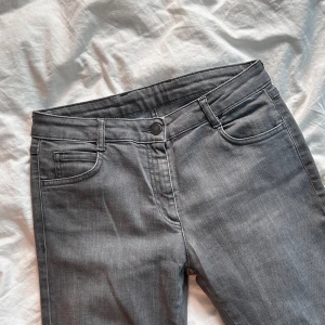 Vintage Grå jeans från MM6 Maison Margiela - Snygga grå jeans från MM6 Maison Margiela med klassisk femficksdesign och raka ben. Jeansen har en mörkgrå ton, bälteshällor och knappstängning fram. Materialet är mjukt denim som sitter bekvämt och passar till många olika stilar.