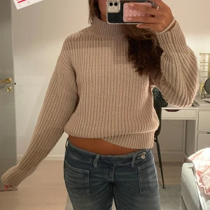 Beige ribbad stickad polotröja - Säljer en beige stickad polotröja med ribbad struktur och hög hals. Perfekt att matcha med jeans eller kjol för en snygg look. Supermysig och stilren färg som passar till allt.
