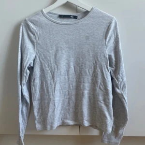 Ljusgrå långärmad tröja - En enkel och stilren ljusgrå långärmad tröja från 157 i storlek M. Tröjan har rund hals och är gjord i mjuk bomull med diskret ribbad struktur. Perfekt för chill dagar eller när du vill ha en clean look. Har två små fläckar. 