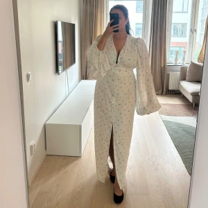 Adoore Positano klänning - Superfin vit Adoore långklänning med små blå blommor, puffiga långärmar och v-ringad hals. Aldrig använd, prislappar sitter kvar. Nypris 1695kr, Storlek 42 (liten i storleken)