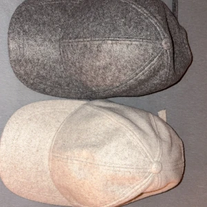 Grå och beige ullkepsar - Två stilrena kepsar i klassisk modell, en i mörkgrå och en i ljusbeige färg. Båda är tillverkade i mjuk ull och har en rundad form med knapp på toppen och justerbar rem baktill. Perfekt för dig som vill ha en clean look med lite vintagevibe :)  Lager 157