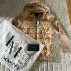 Beige pufferjacka från Leon Marcel - Nypris 1350kr, denna är aldrig använd! Säljer på grund av att den inte passade. Annars en sjukt snygg beige pufferjacka från Leon Marcel med stickade ärmar och huva. Jackan har quiltad framsida i syntetmaterial, dragkedja och två fickor med zip. Baksidan och ärmarna är stickade för extra komfort och stil. Perfekt för dig som gillar en chill och modern look. 