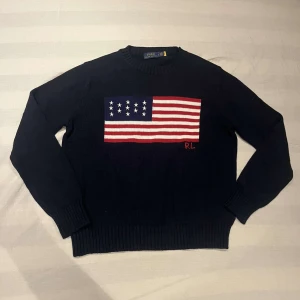 Mörkblå stickad tröja Polo Ralph Lauren usa - Säljer en mörkblå stickad tröja från Polo Ralph Lauren i storlek L. Tröjan har ett stort amerikanskt flaggmotiv på bröstet med RL-broderi i rött. Rund hals och ribbade muddar vid ärmar och nederkant. Perfekt för dig som gillar klassisk preppy stil. Säljer pga av att jag försöker byta stil. Om ni undrar något är det bara att fråga. Priset är inte hugget i sten