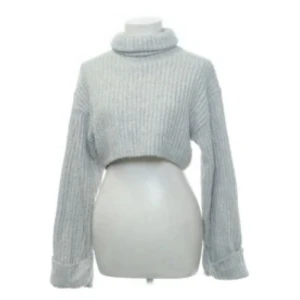 Grå croppad polotröja Gina Tricot - Supermjuk och ribbad grå polotröja från Gina Tricot. Croppad modell med lång ärm och hög polokrage, perfekt för lager på lager. Stickad i ett mysigt material som håller dig varm under kyliga dagar.