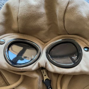 Beige hoodiejacka med goggles C.P. Company - Säljer en beige hoodiejacka från C.P. Company med ikoniska goggles i huvan. Jackan har hel dragkedja, två fickor med dragkedja och snörning i huvan. Materialet är mjukt bomullstyg och passformen är normal. Nypris 2500kr