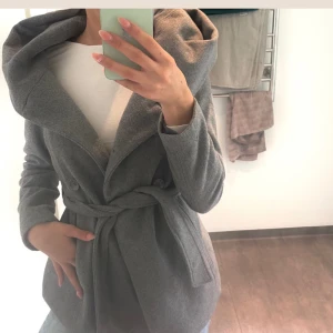 Grå kappa med stor huva och bälte - Snygg grå kappa med stor, draperad huva och knytskärp i midjan.