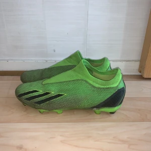 Adidas gröna fotbollsskor strl 42 - Säljer ett par gröna Adidas fotbollsskor i storlek 42 med svart detalj och mönstrad ovandel. Skorna har låg profil, platt sula med dobbar och är tillverkade i syntetmaterial. Snygg design med klassiska tre svarta ränder på sidan och X-logga bak.