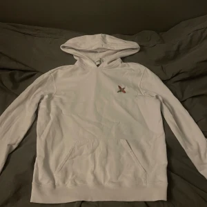 Vit hoodie från Axel Arigato med fågel - Vit hoodie från Axel Arigato med broderad fågel på bröstet. Tröjan har huva, känguruficka och långa ärmar. Mjuk bomullskvalitet och stilren design som passar dig som gillar cleana streetwear-plagg.