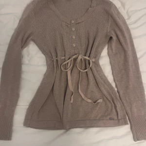 Stickad babydoll tröja  - Världens sötaste och trendigaste abercrombie fitch- liknande stickad babydoll tröja! Med snörning i mitten. Så mjuk och skön, inga defekter. Knapparna går inte att öppna.  En ljusbrun / mörk beige färg. 