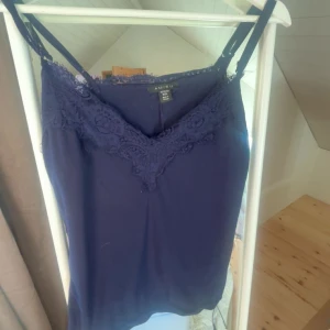 Mörkblå linnetopp med spets från Amisu - Supersnygg mörkblå linnetopp från Amisu med spetsdetaljer längs v-ringningen. Tunn och lätt, perfekt för varma dagar eller att styla lager på lager. Justerbara smala axelband för bästa passform. Är i xl men passar som s eller m